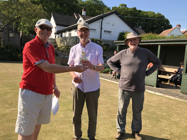 Three men standing on the green, posing with the trophy.