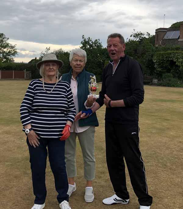 Two women and man posing on the green with the small trophy.